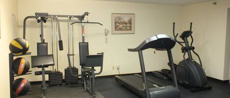 A gym with exercise equipment including a treadmill, elliptical, and weight machines.