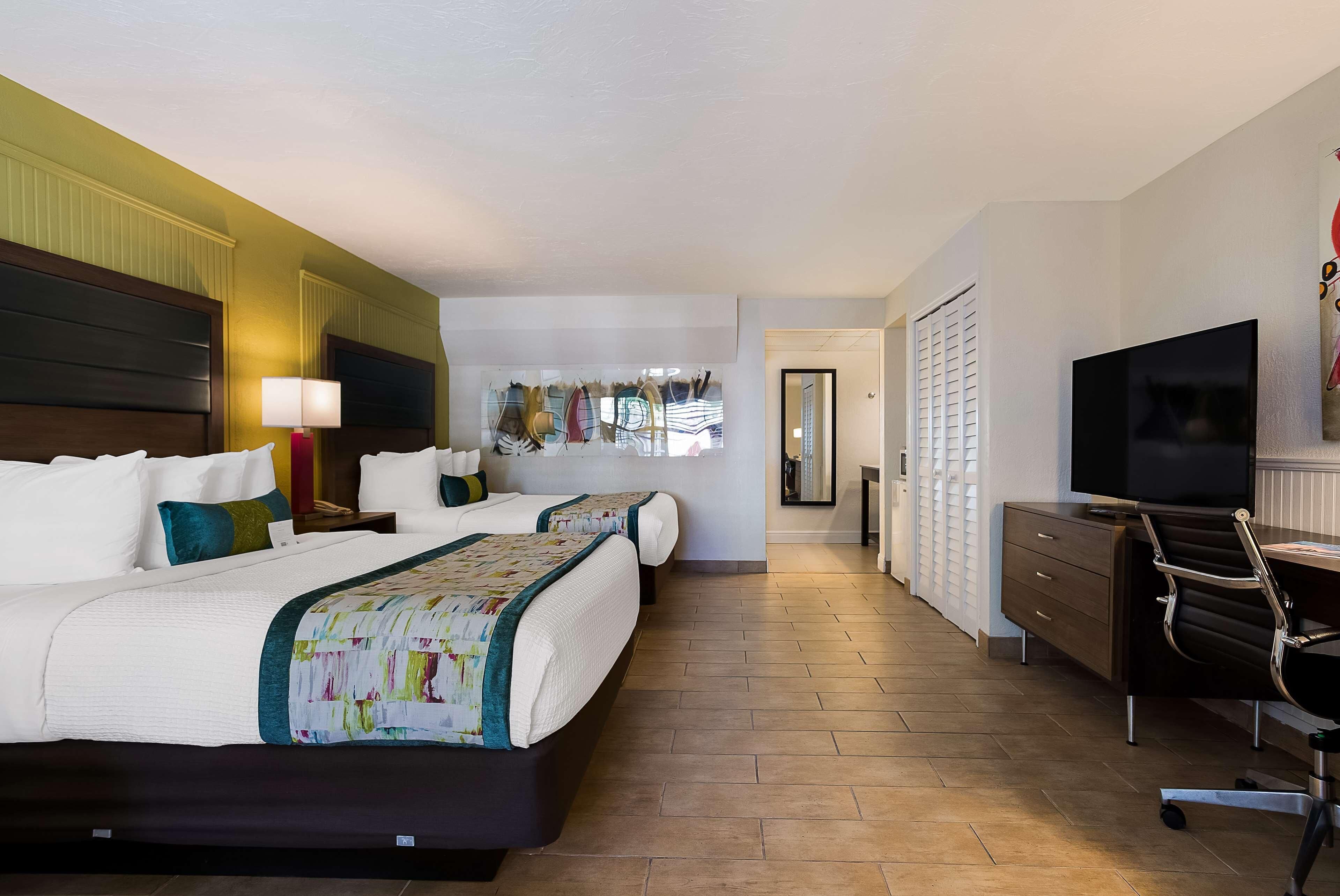 A hotel room with two beds, a desk with a chair, a TV, and a wardrobe.