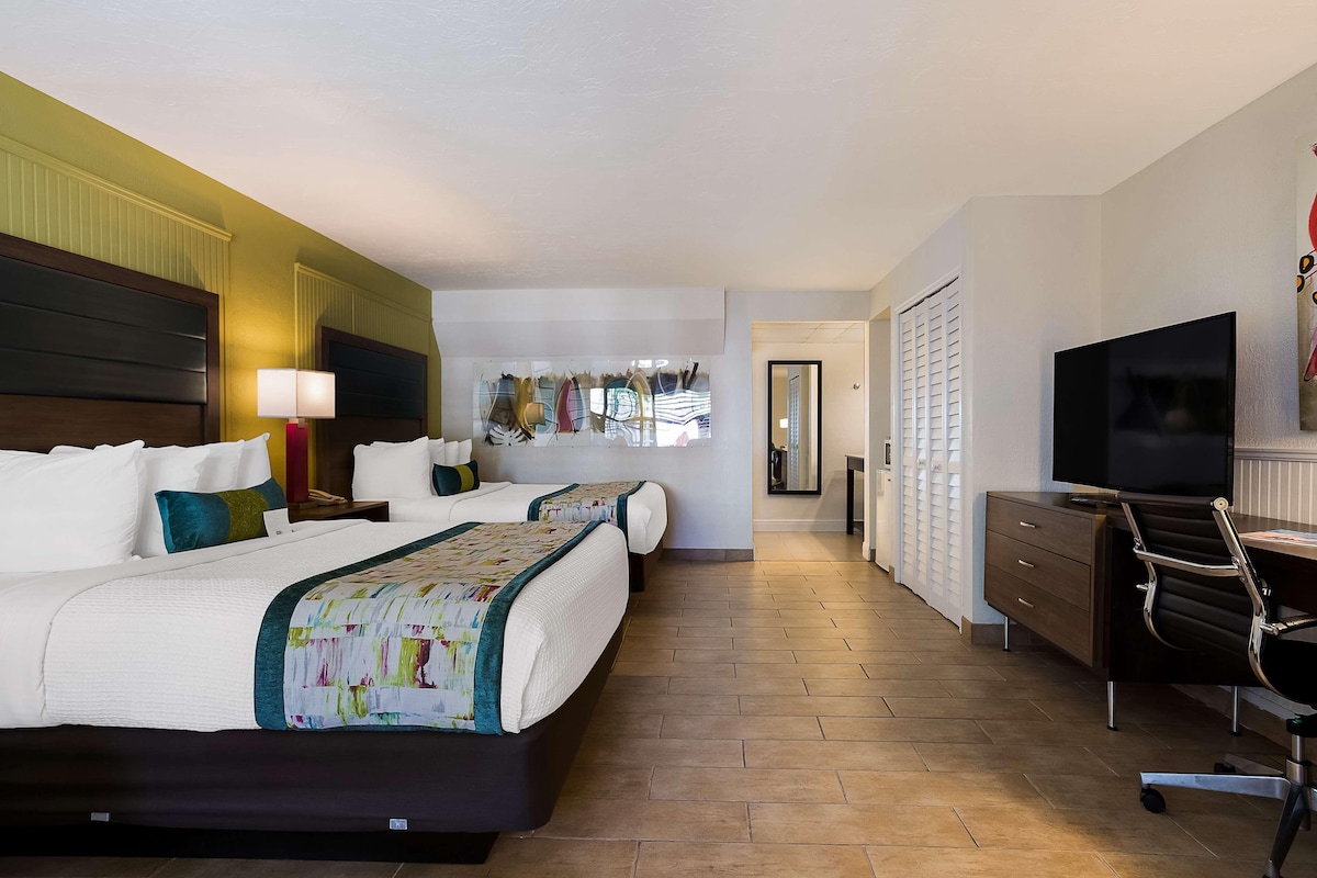 Een hotelkamer met twee bedden, een bureau met stoel, een televisie en een kledingkast.