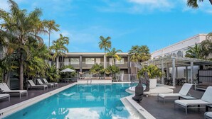 A swimming pool with lounge chairs and palm trees, surrounded by a building with a covered patio area. - Best Western Hibiscus Motel (Key West)