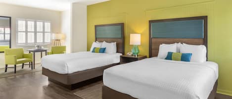 A hotel room with two beds, a desk, a chair, and a window.