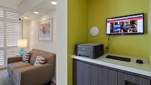 Zona de recepción con un monitor de computadora mostrando un sitio web, una impresora, un teclado y un sofá con cojines de colores.
