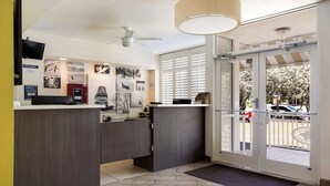 A reception area with a counter, wall-mounted artwork, ceiling fans, and a large window with blinds. - Best Western Hibiscus Motel (Key West)