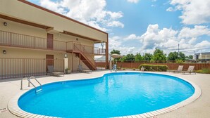 A swimming pool with a tiled deck, a staircase leading to a balcony, and outdoor seating.