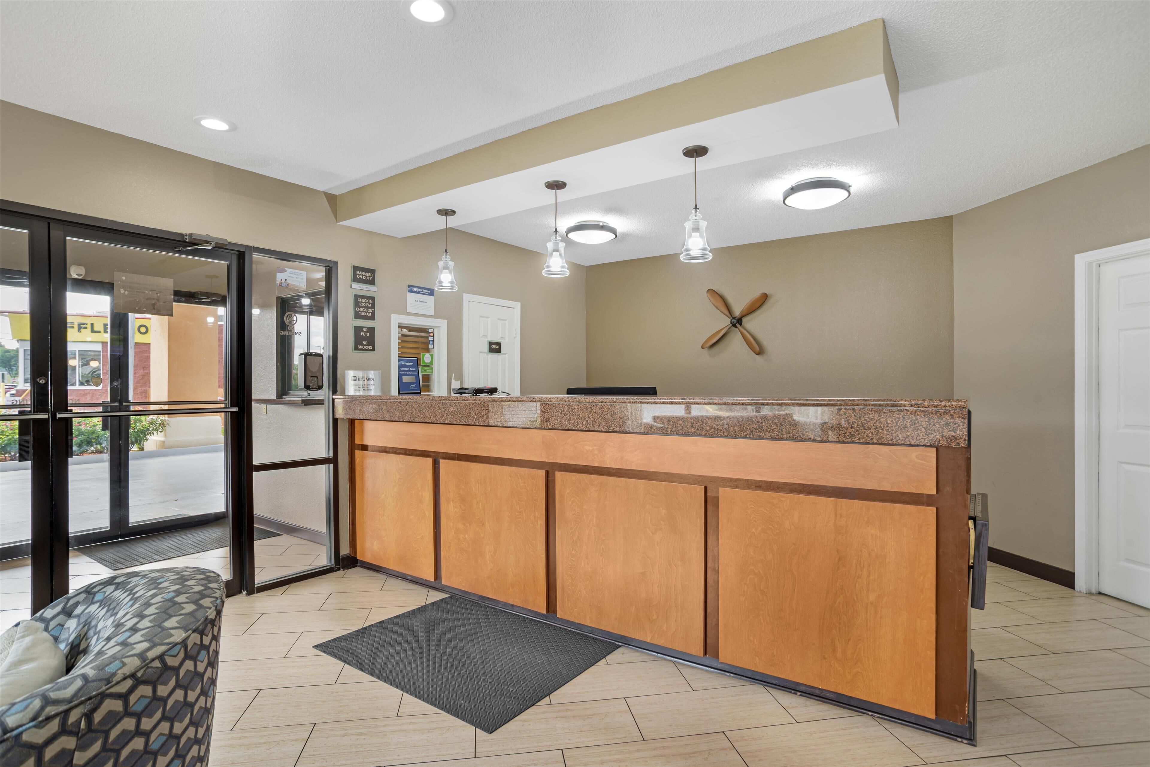 A reception area with a wooden counter, glass doors, a patterned sofa, and a ceiling fan.