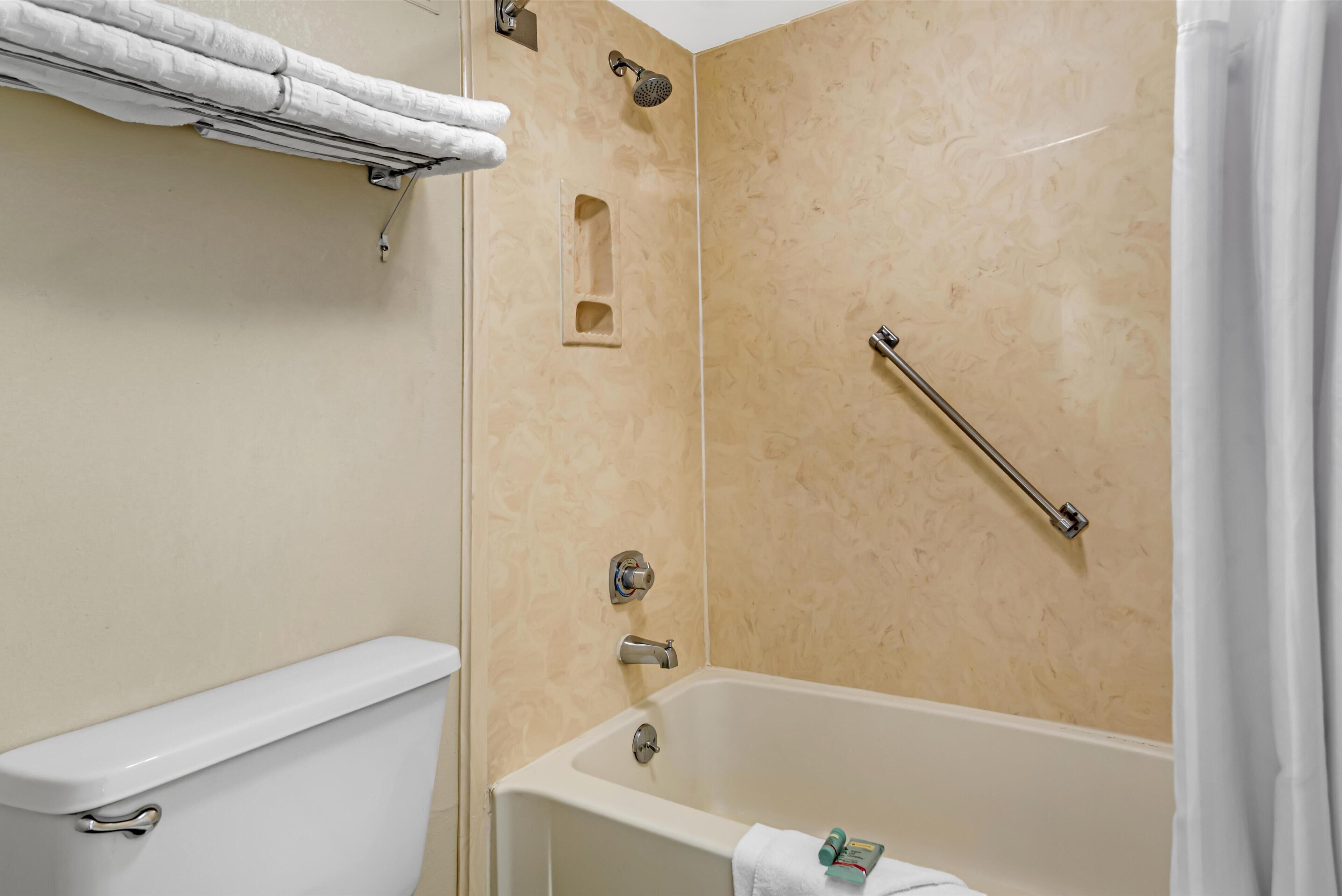 Un bagno con un WC, una doccia dotata di maniglione e una vasca da bagno con un asciugamano.