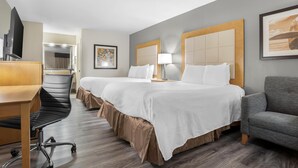 A hotel room with two beds, a desk, a chair, a TV, and a lamp.