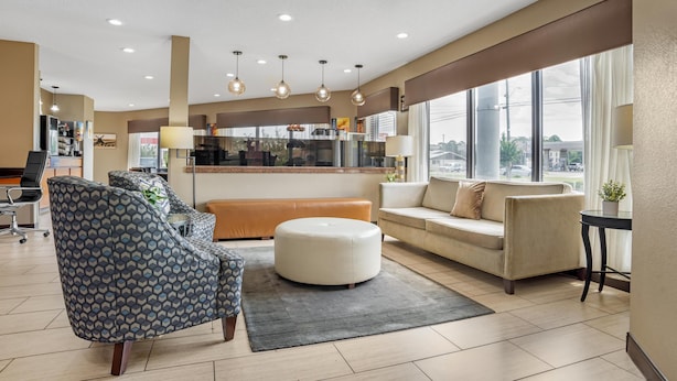 A modern hotel lobby with a sofa, armchair, ottoman, and a dining area with a counter and chairs.