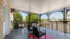 A covered balcony with two chairs, a red mat, and a decorative metal railing. - Super 8 by Wyndham New Orleans (New Orleans)