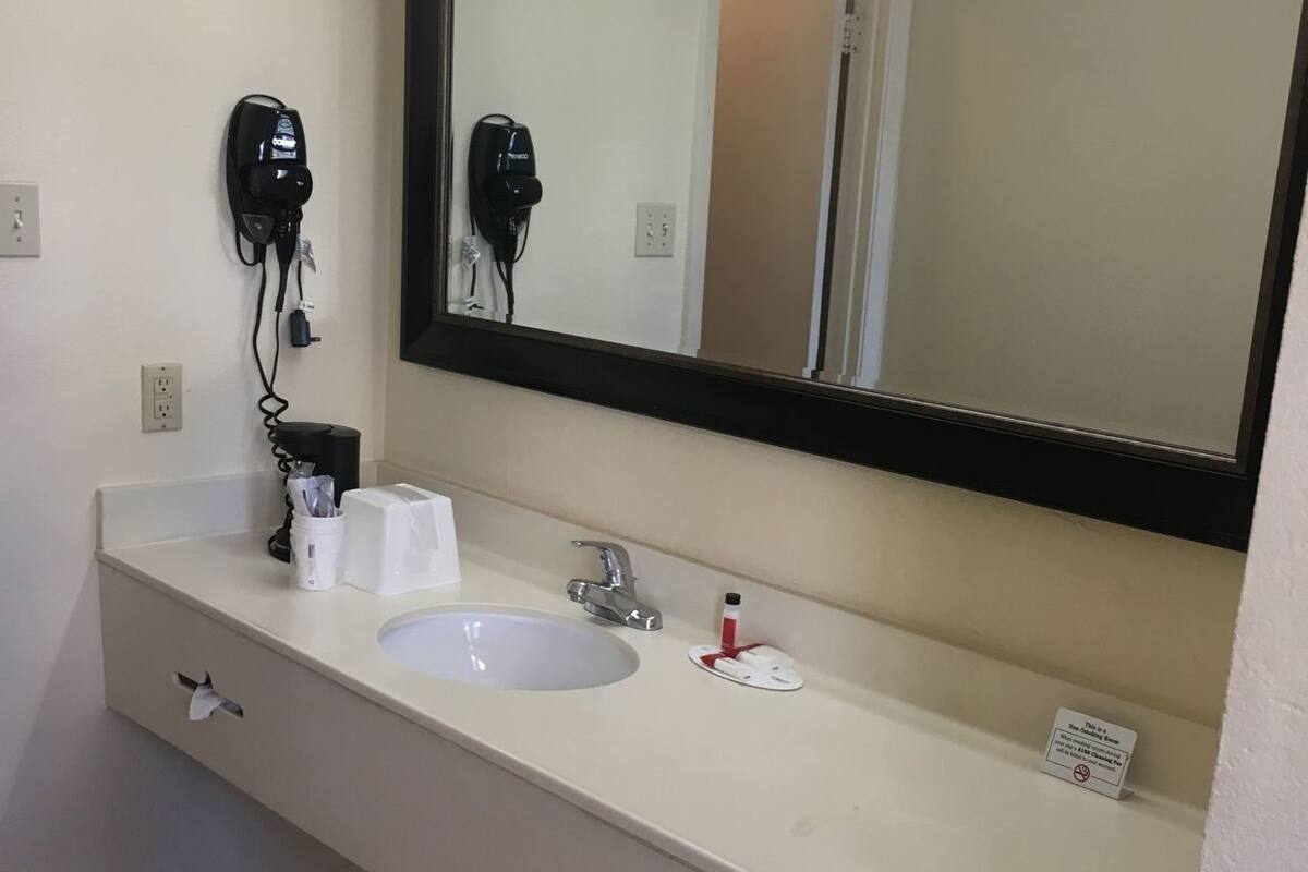 Une salle de bain avec un lavabo blanc, un miroir, un sèche-cheveux et un porte-serviettes.