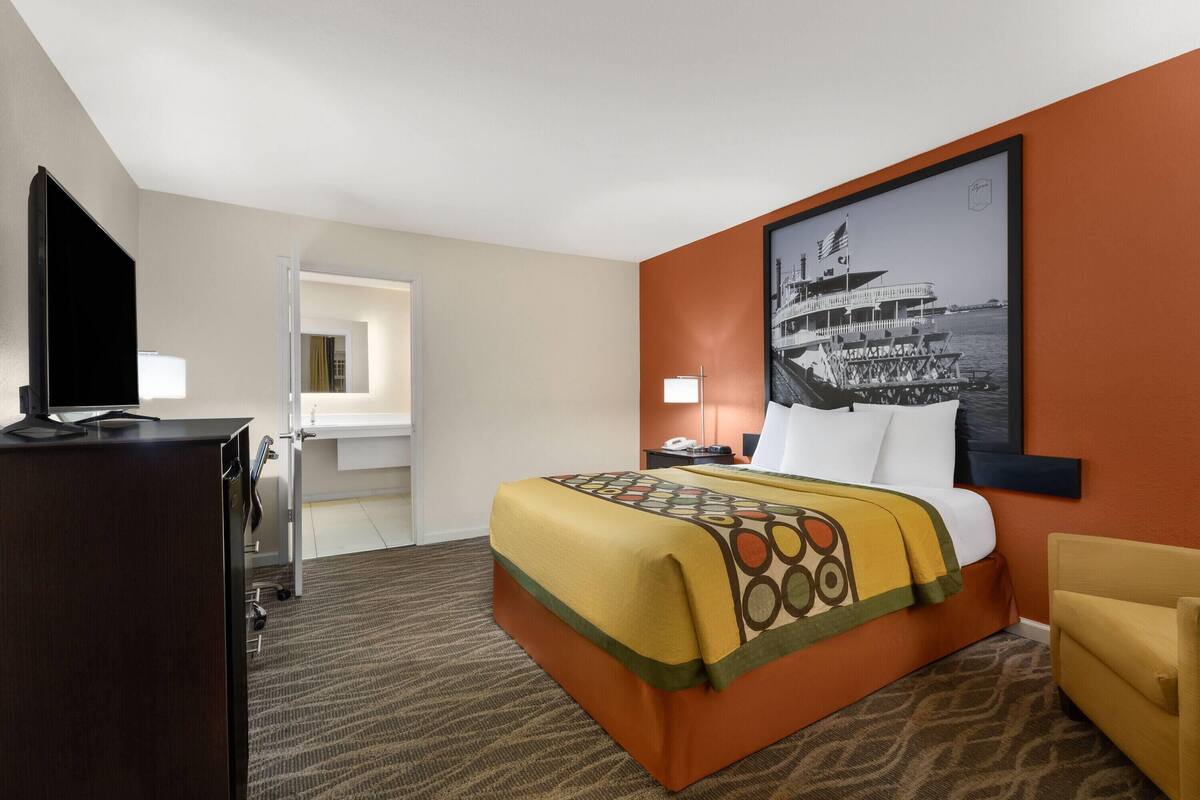 Une chambre d’hôtel avec un lit, un bureau, une télévision, une salle de bain et une grande fenêtre.