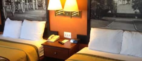 A hotel room with two beds, each with a patterned bedspread, a nightstand with a lamp, and a wall-mounted telephone.
