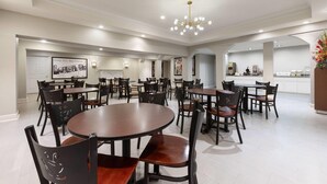 A spacious dining area with multiple round tables and chairs, a modern chandelier, and a kitchen area in the background. - Super 8 by Wyndham New Orleans (New Orleans)