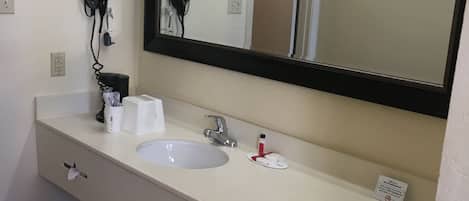 A bathroom with a white sink, a mirror, and a hairdryer mounted on the wall.