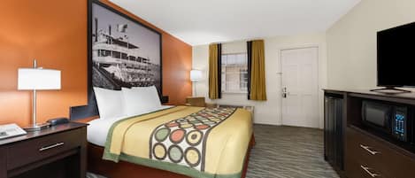 Habitación de hotel con cama, escritorio con lámpara, televisión y un cuadro grande en la pared.