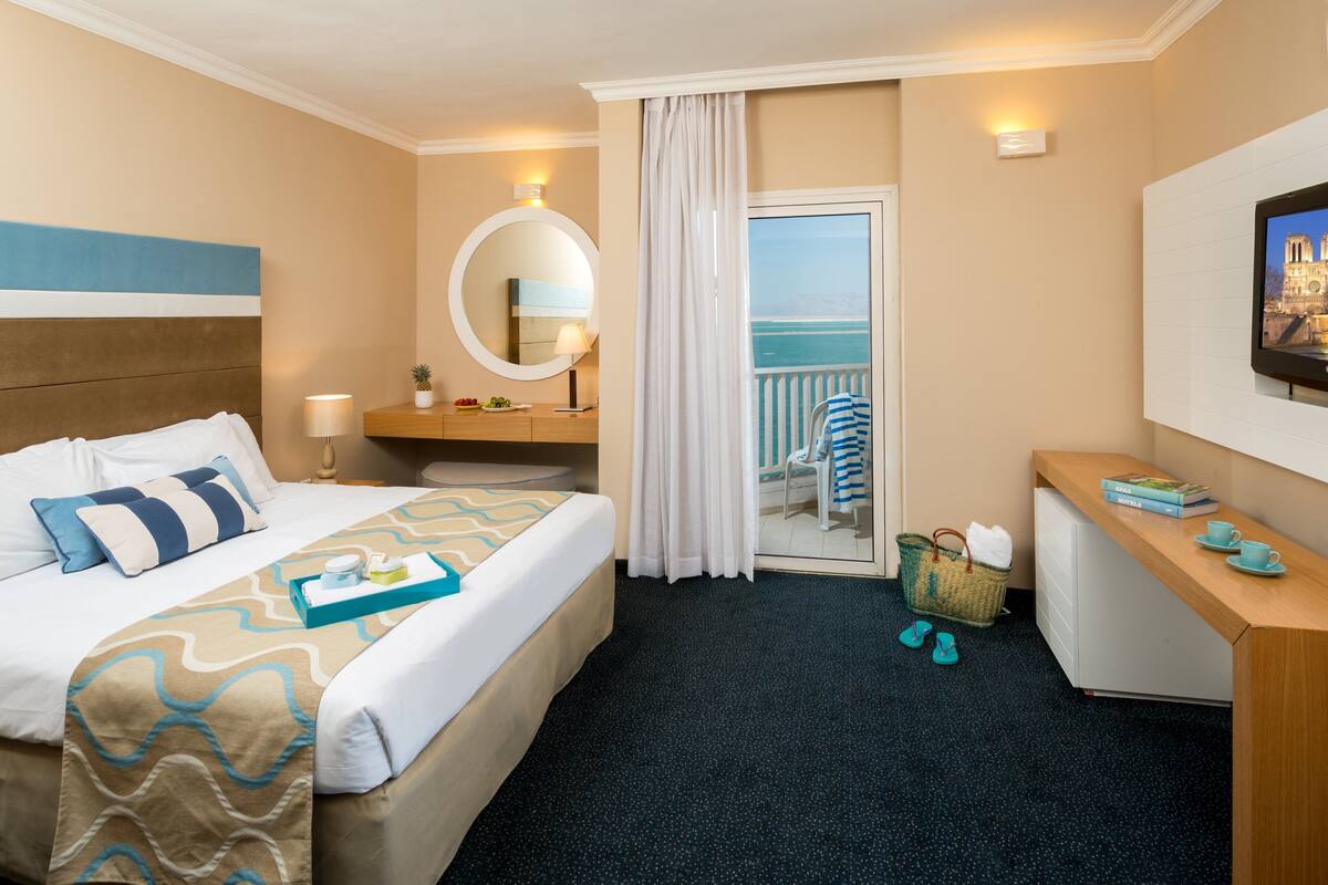 Habitación de hotel con cama, mesita de noche, televisor y vista al mar.