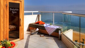 Ein Balkon mit einer Rattan-Couch, einer Holztür mit der Aufschrift "Dolphin Spa" und Blick aufs Meer.