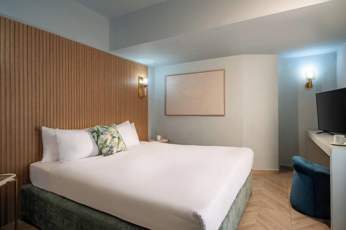 Una habitación de hotel moderna con una cama grande, cabecera de madera, televisor de pantalla plana y escritorio con silla.