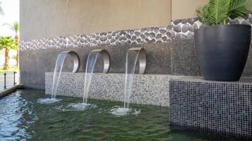 A water feature with three curved spouts, a large planter, and a tiled wall with a pebble pattern.