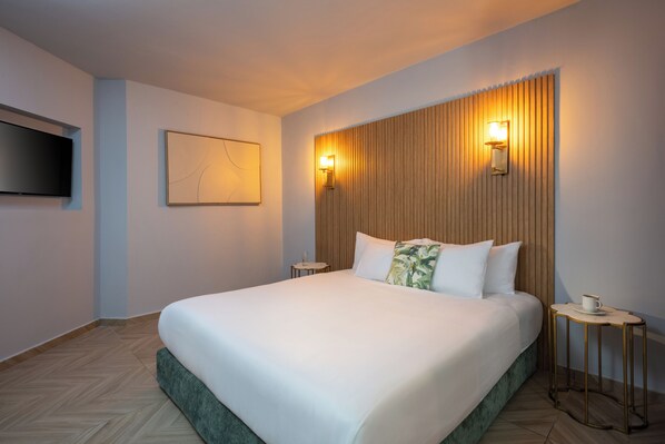 A neatly made bed with white linens, a small bedside table with a cup, and a wall-mounted TV. - Leonardo Club Hotel Dead Sea (Tamar)