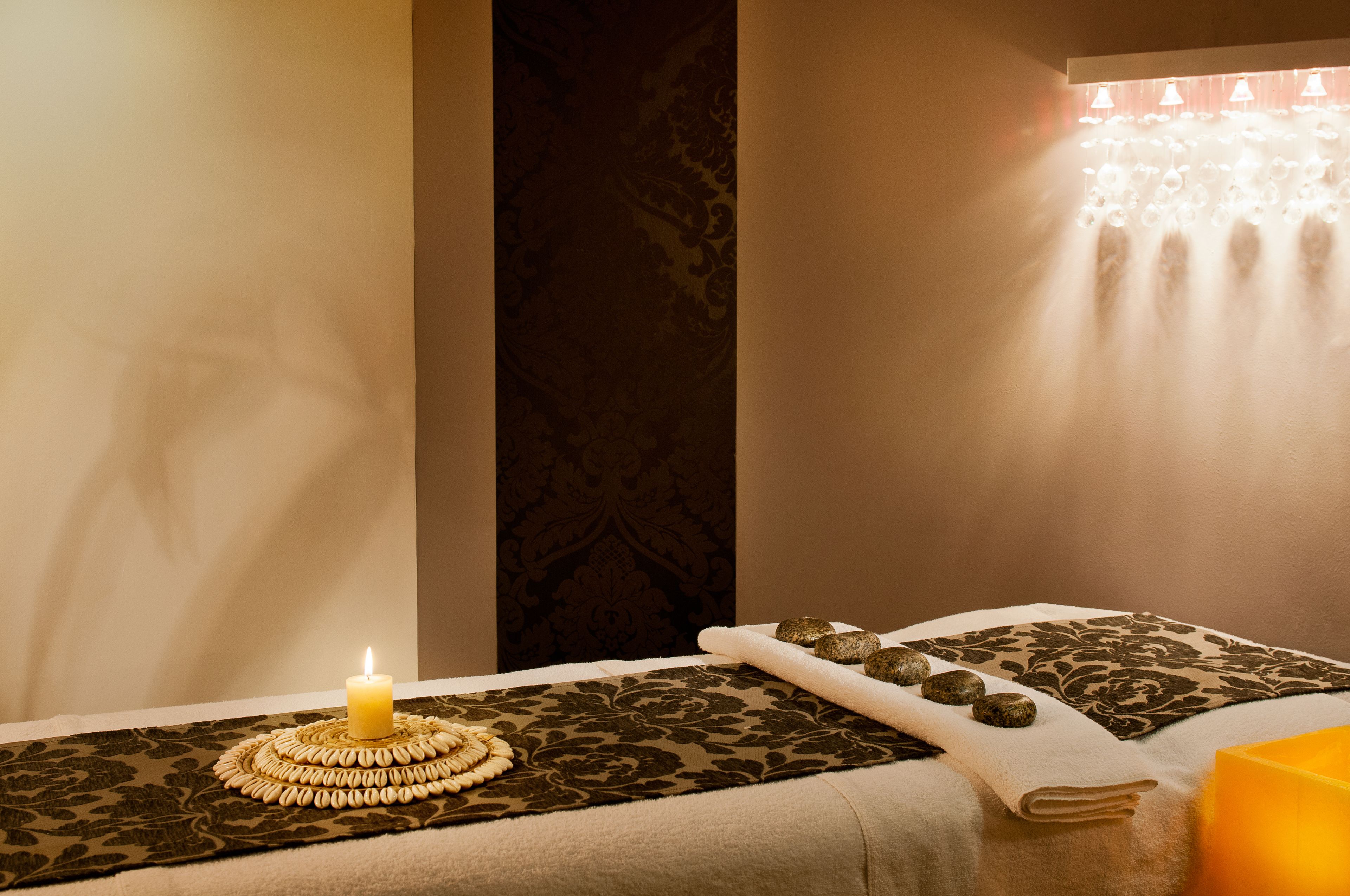 A spa room with a bed, a lit candle, a decorative mat, and a wall with a water feature.