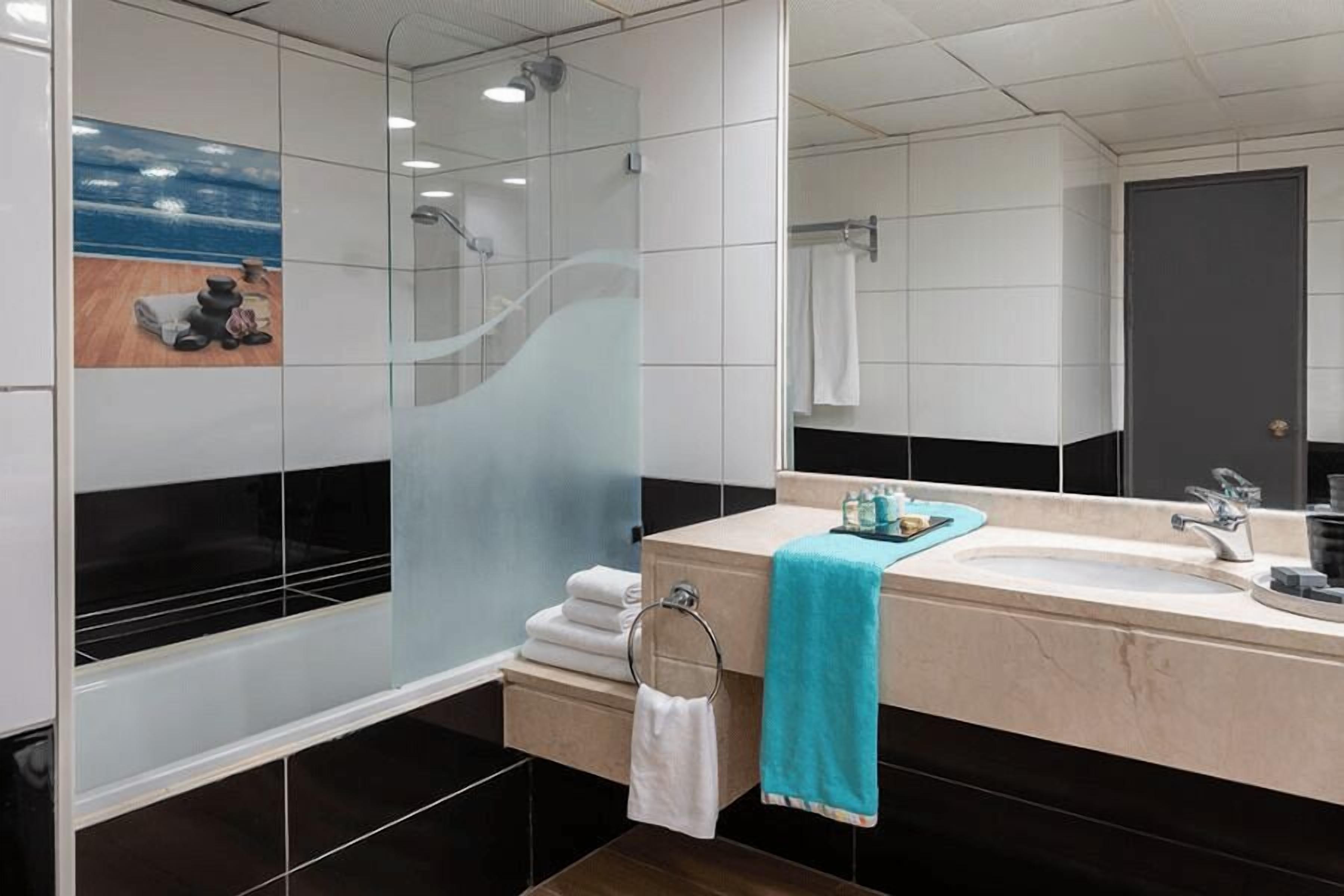 Un baño moderno con ducha envuelta en vidrio, un espejo grande y un tocador color crema con lavamanos y toallero.