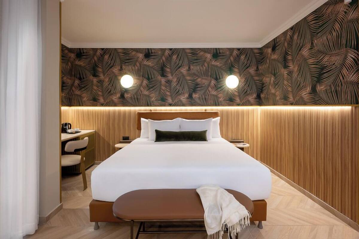Una habitación de hotel con cama, mesitas de noche, un escritorio y un banco.
