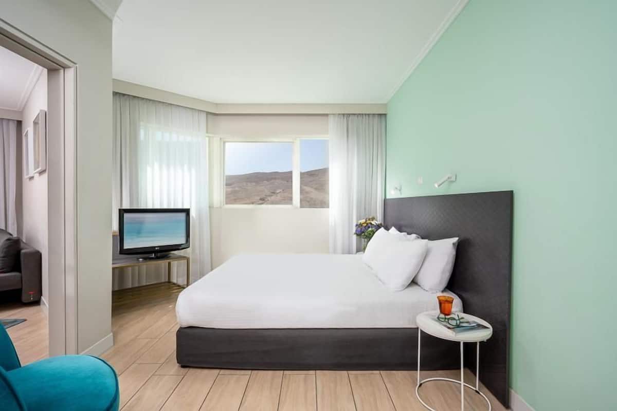 Habitación de hotel moderna con una cama grande, un televisor, una mesita con una bebida y vistas al exterior.