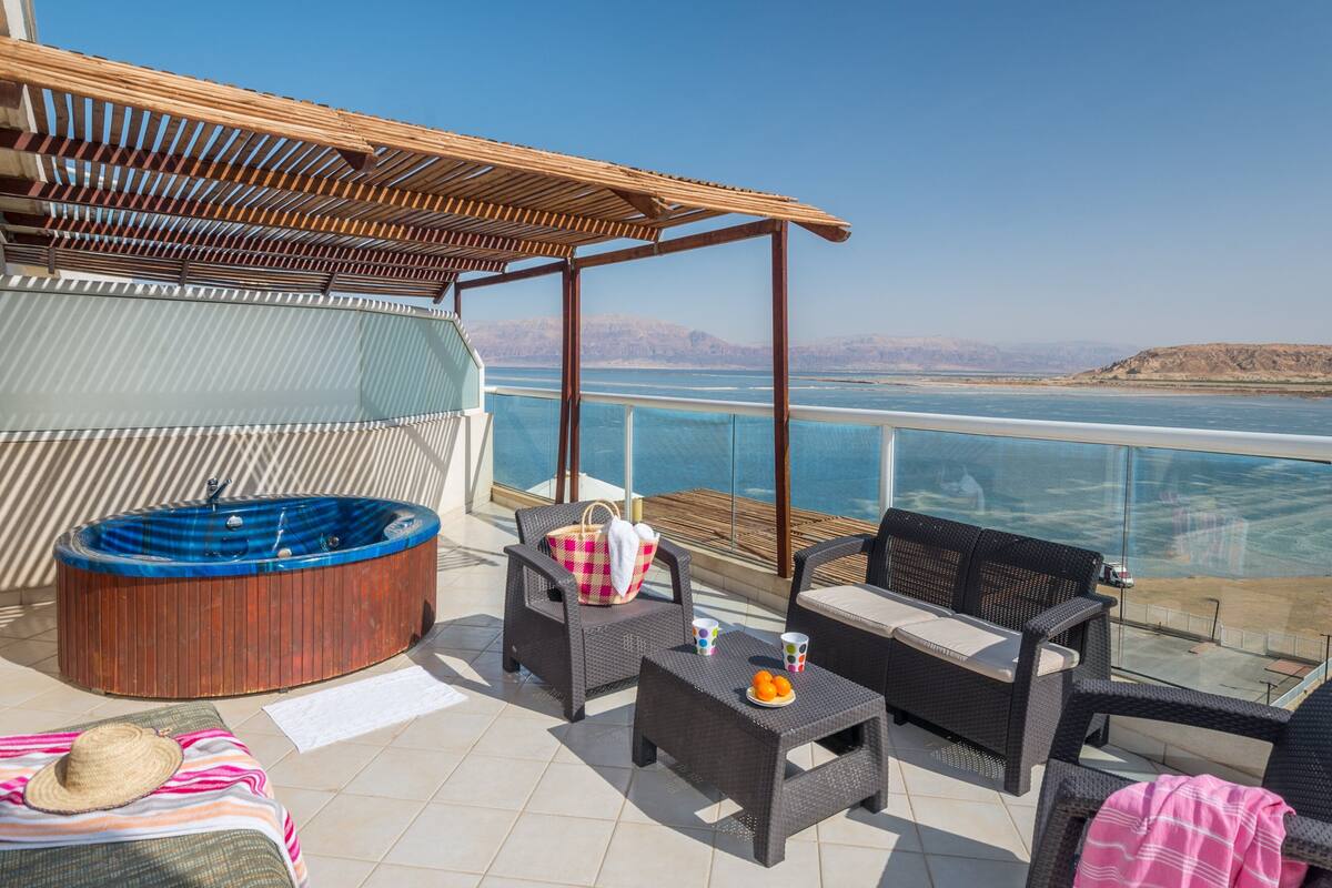 Un balcón con mobiliario de mimbre, una bañera de hidromasaje y vista al mar.