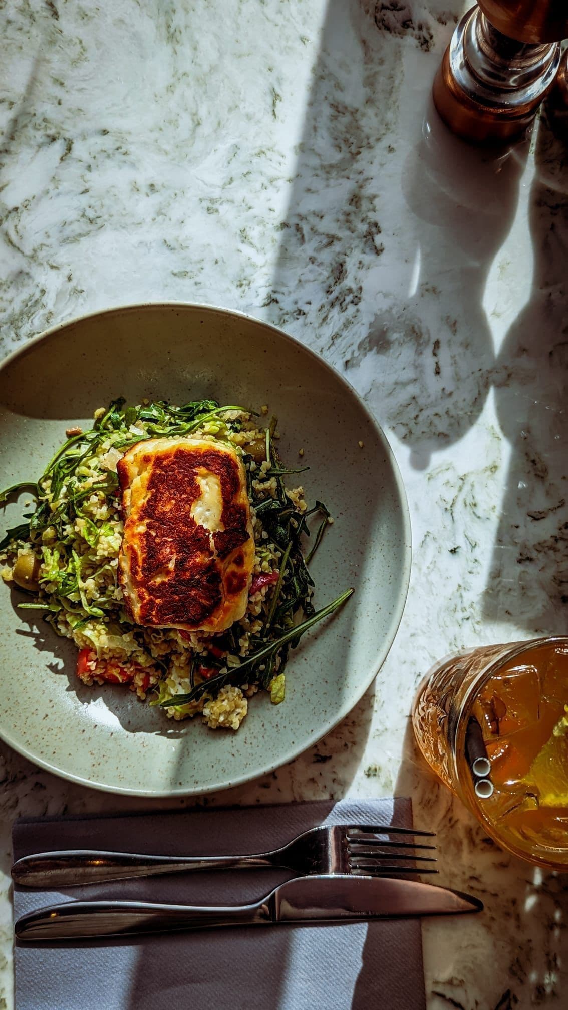 A plate of food with a piece of grilled meat and greens, accompanied by a fork and knife on a napkin.