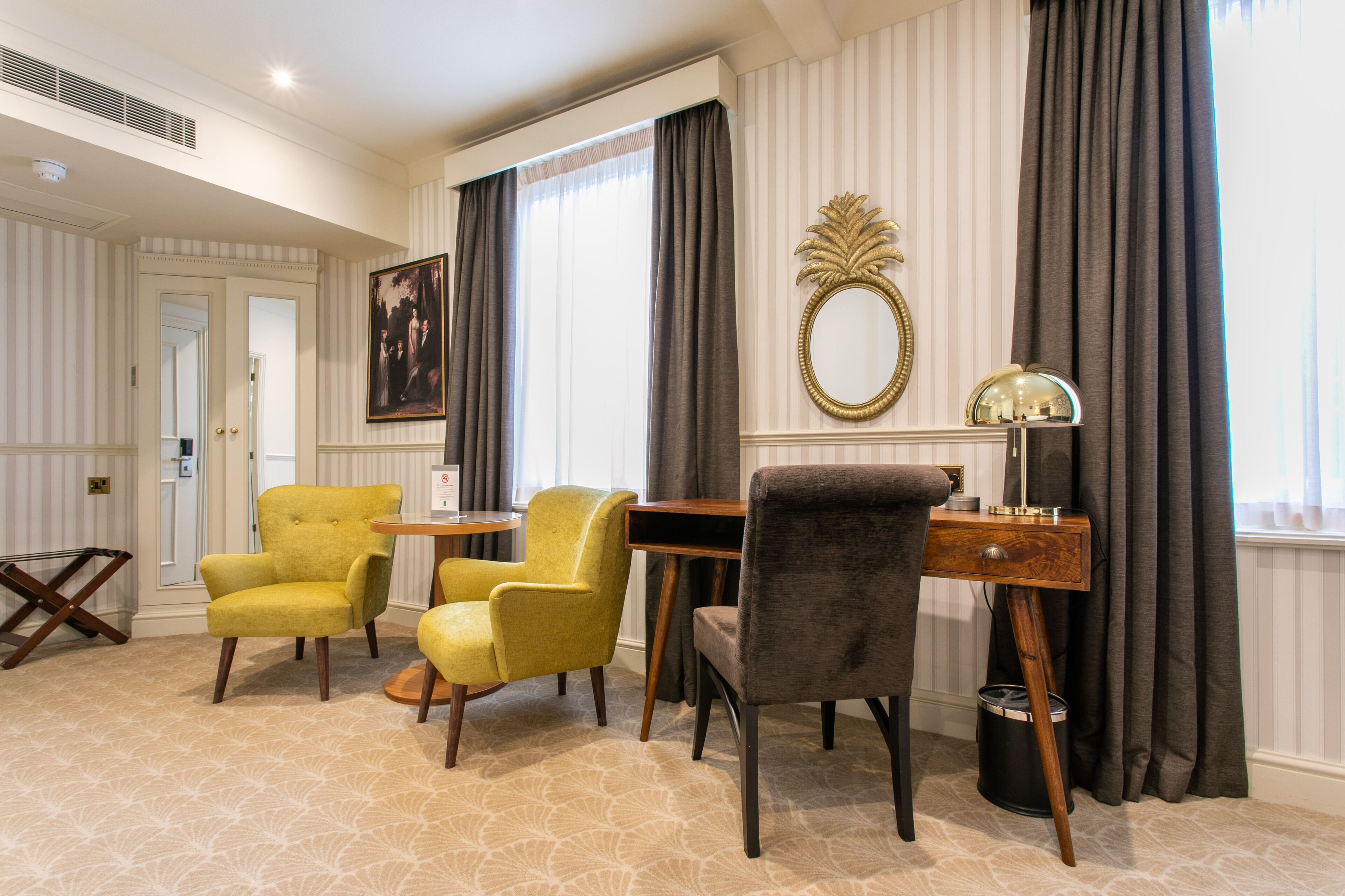 A room with a desk, two yellow chairs, a grey chair, a mirror, and a lamp.
