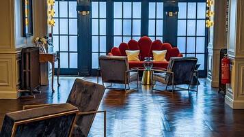 A spacious lobby with a red sofa set, marble chairs, and a chandelier.