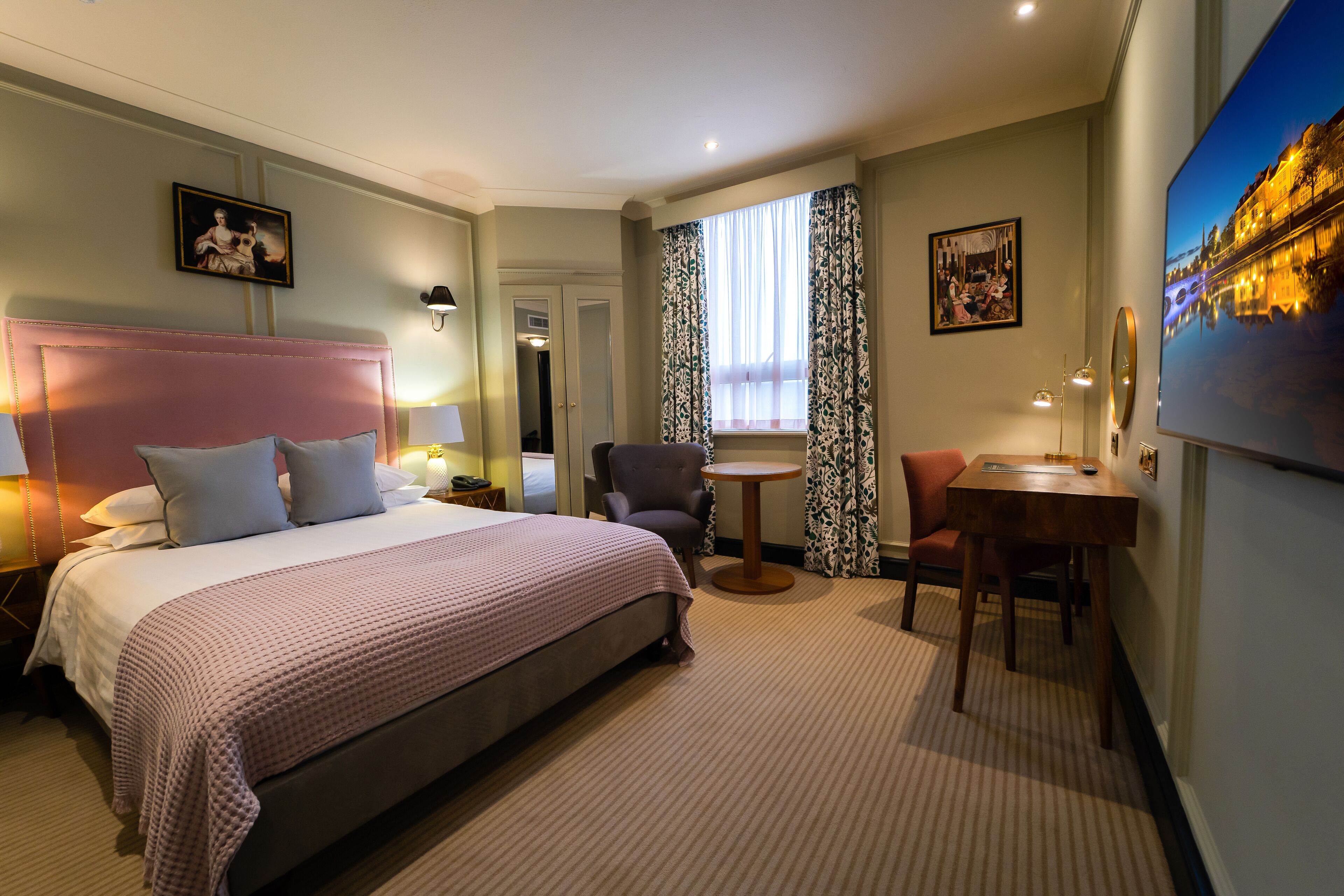 A hotel room with a large bed, a round table, a chair, and a TV on the wall.