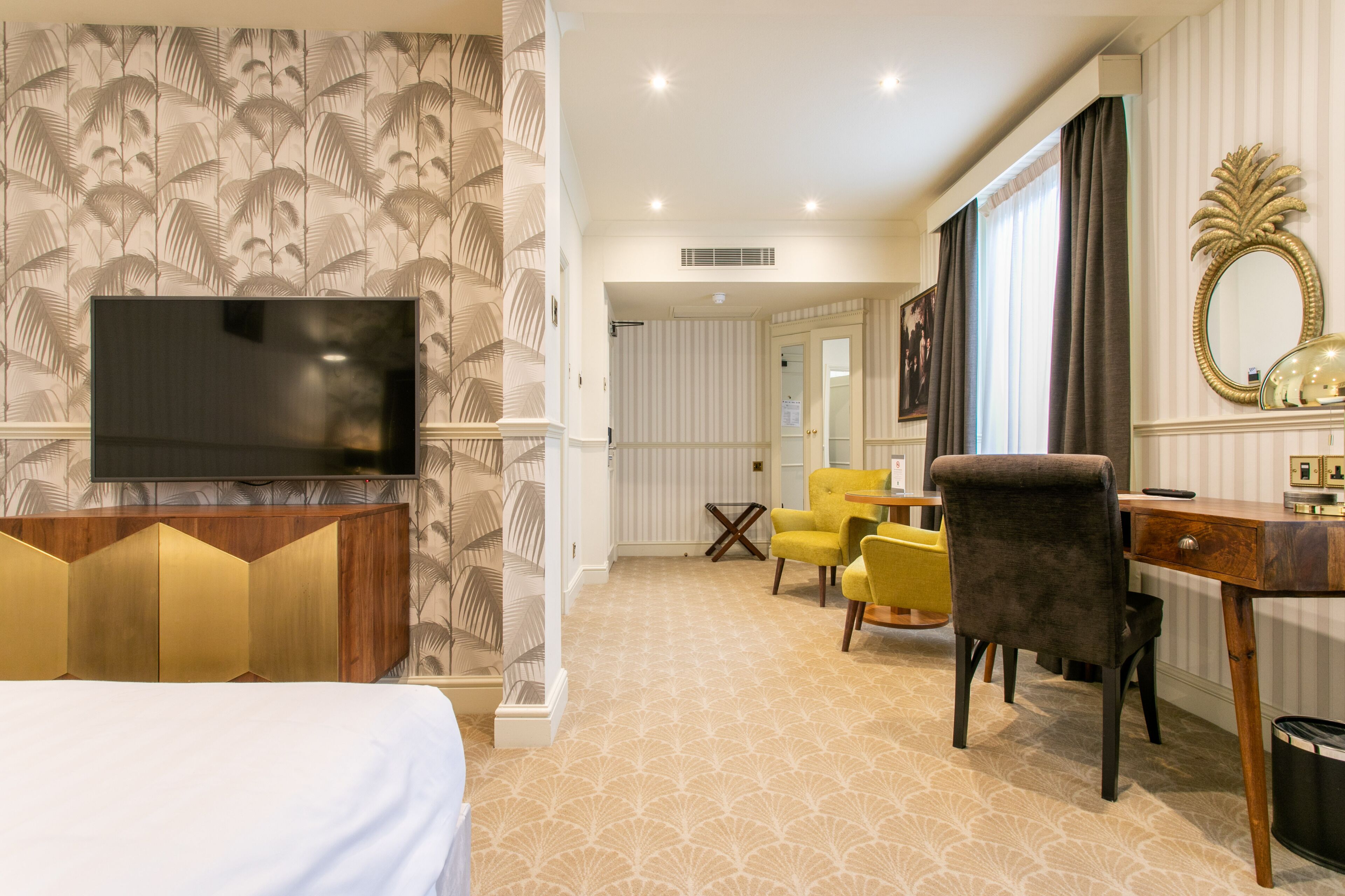 A hotel room with a bed, a TV, a desk with a chair, and a large mirror.