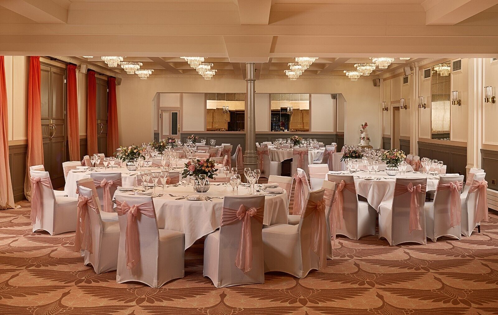 A banquet hall with round tables, white tablecloths, and chairs with pink sashes.