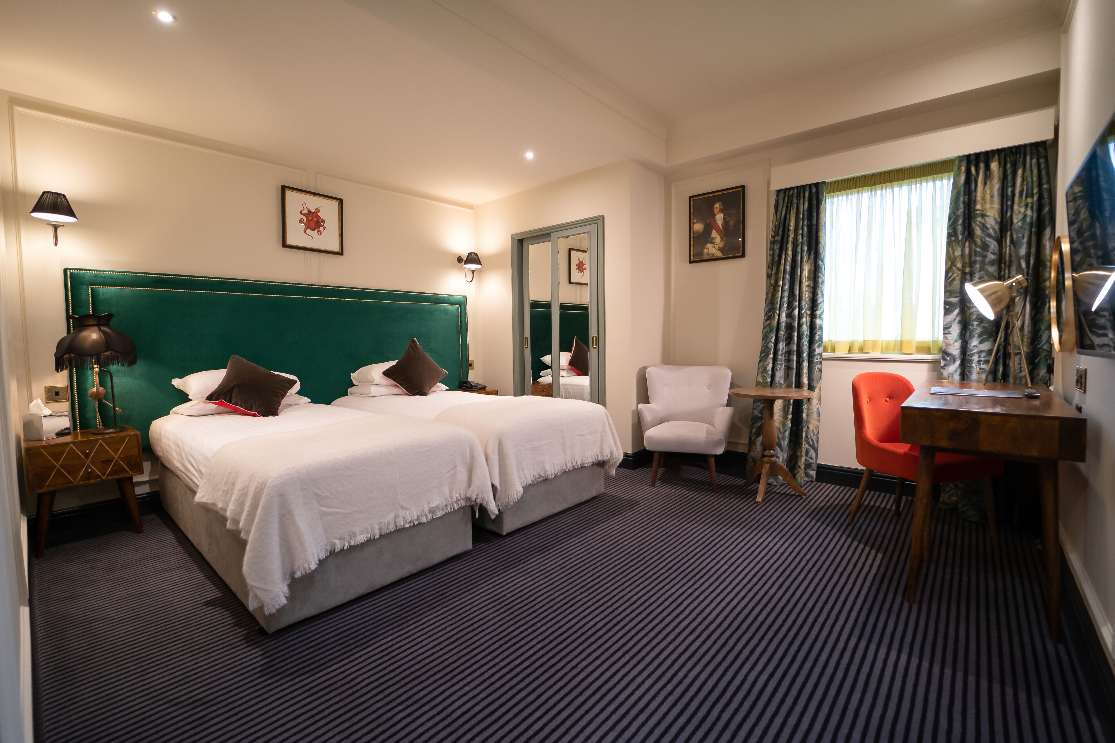 Habitación de hotel con dos camas, un escritorio, una silla, una lámpara y una ventana con cortinas.