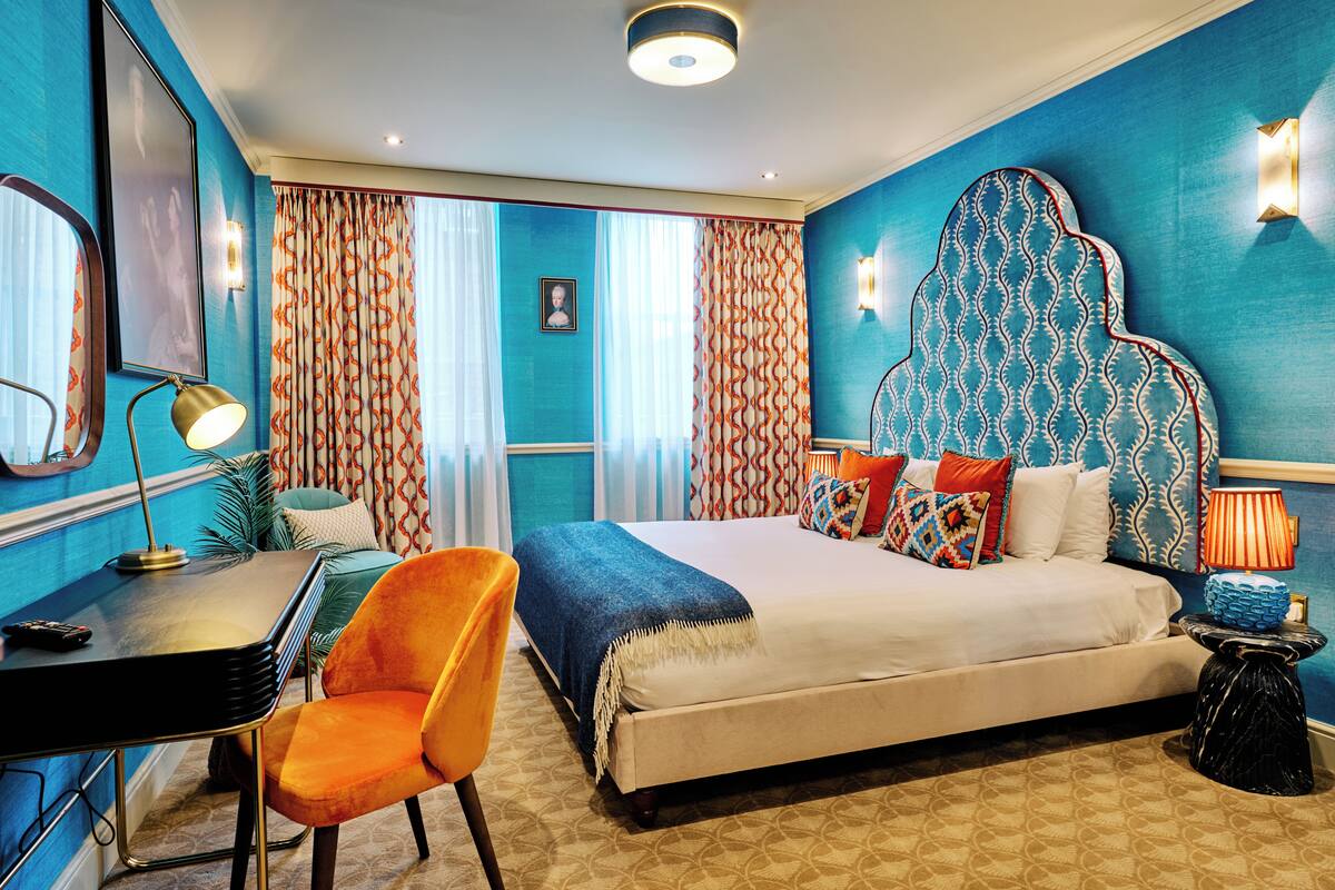 Una habitación de hotel con una cama grande, un escritorio, una silla naranja y un cabecero estampado.