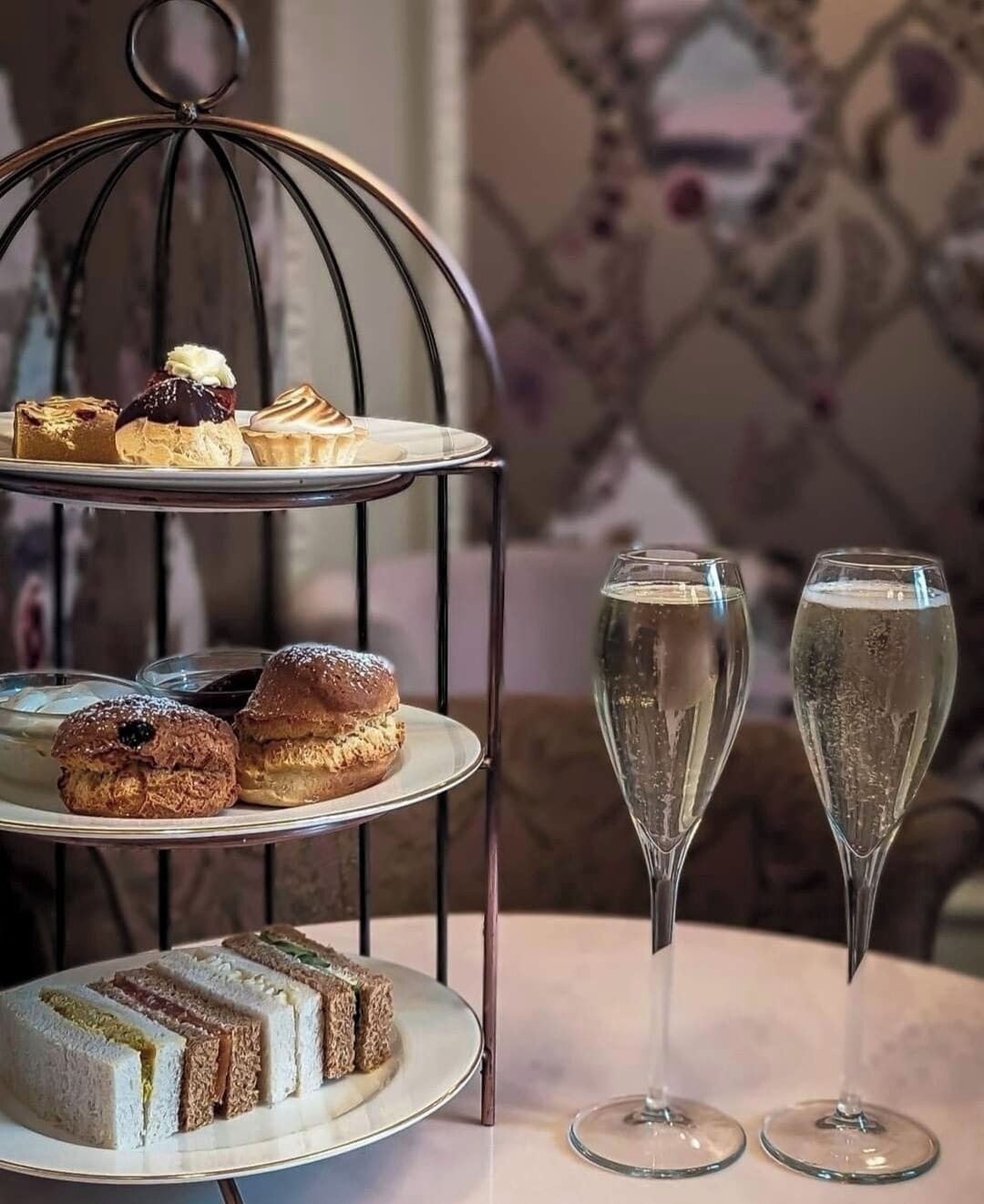 Un soporte para postres de tres niveles con varios pasteles y una mesa con dos copas de champán.