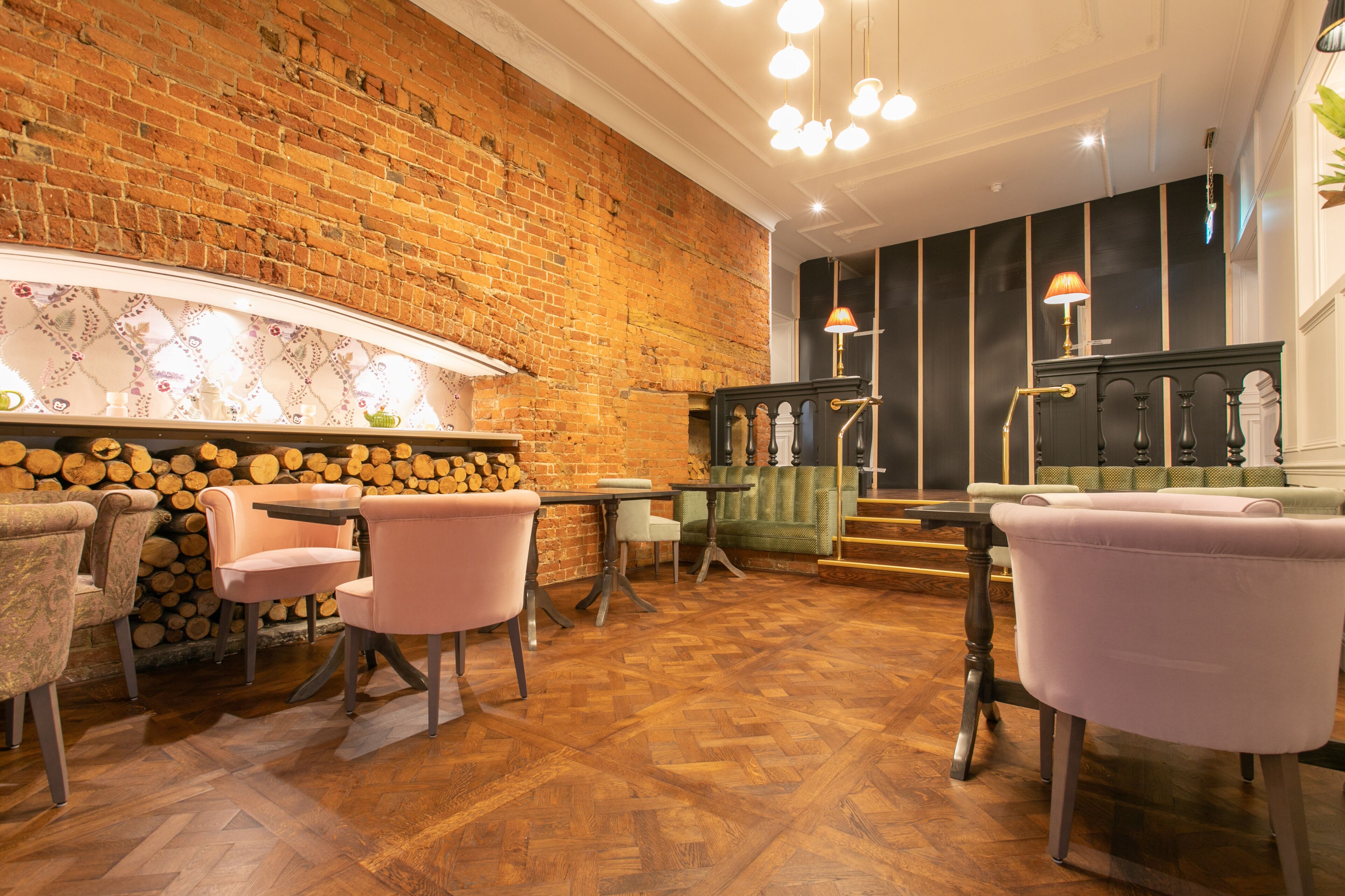 Un interior acogedor con pared de ladrillo, suelo de parquet de madera y una zona de estar con sillas rosas y sofá verde.