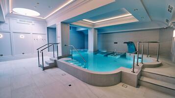 Piscina interior moderna con agua cristalina, rodeada de escalones y barandillas, y un suelo de baldosas.
