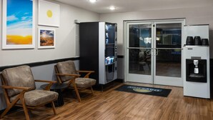 A room with wooden flooring, two chairs, a refrigerator, a vending machine, and a door leading outside.