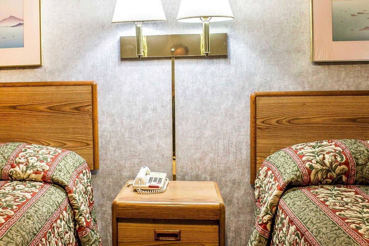 A hotel room with two beds, a bedside table with a telephone, and two wall-mounted lamps.