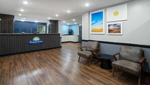 A reception area with a reception desk, wooden flooring, two chairs, a small table, and framed pictures on the wall.