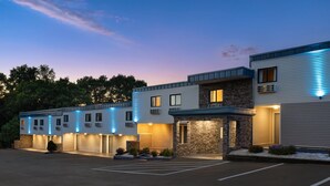 A multi-story hotel with a parking lot in front, featuring a modern architectural style with stone accents and blue ambient lighting.