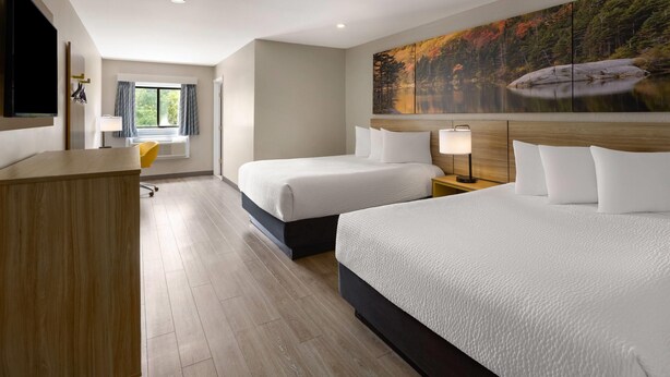 A hotel room with two beds, a desk, a chair, a TV, and a painting of a lake.