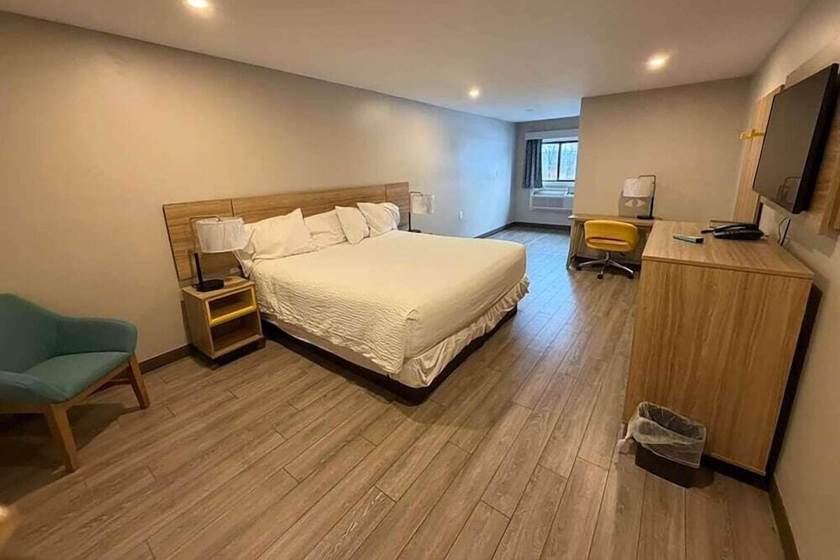A hotel room with a large bed, a desk with a chair, a TV, and a window.