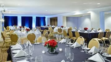 A banquet hall with round tables set for dining, featuring gold chairs and white tablecloths.
