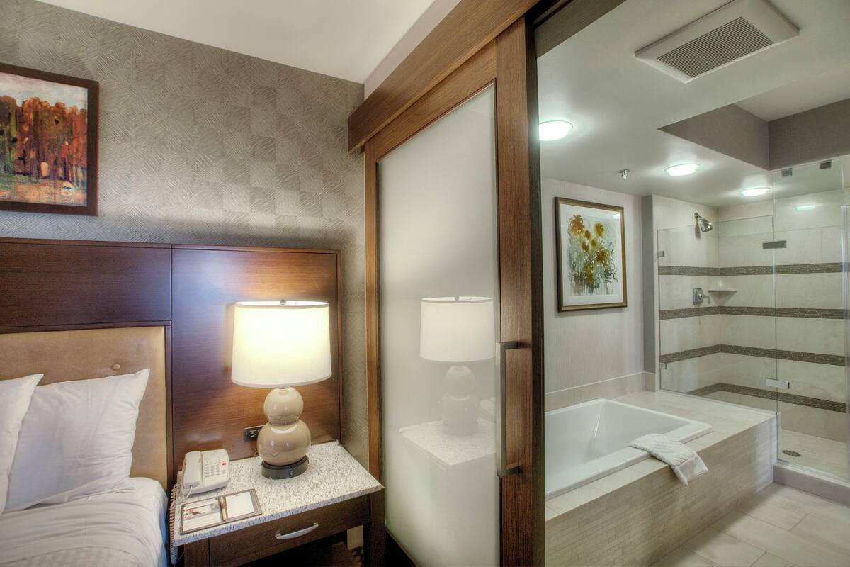 A hotel room with a bed, bedside lamp, phone, and a painting on the wall.
