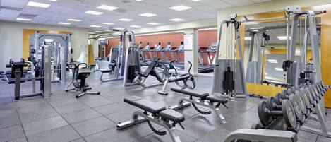 Un gimnasio con diverso equipo de ejercicio, incluyendo cintas de correr, máquinas de pesas y bancos.