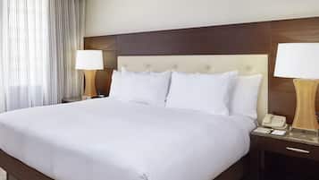 A large bed with white linens, two bedside tables with lamps, and a wooden headboard.